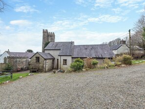 A stone building with a tower, gravel driveway, and a bench.