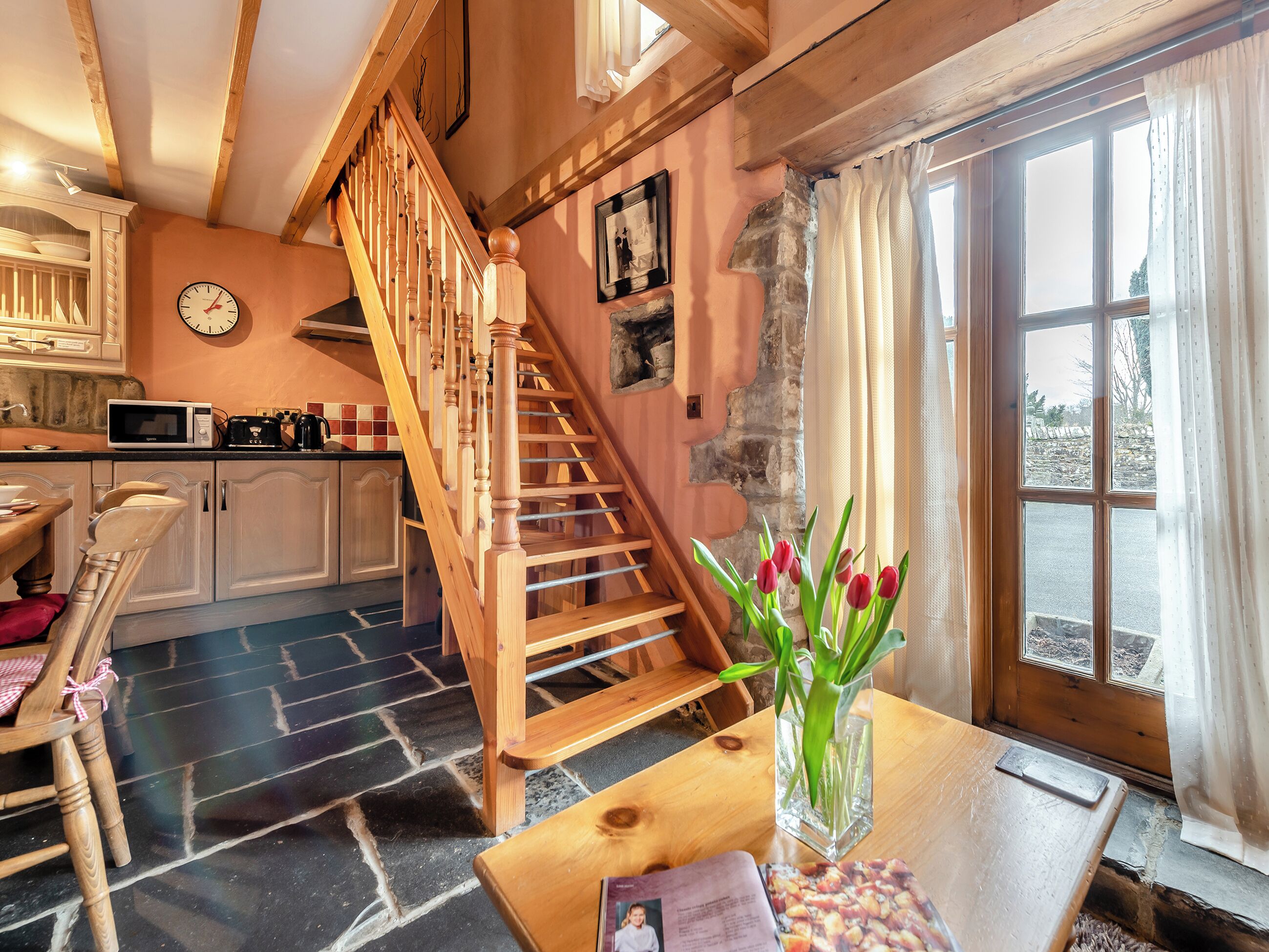 Eine rustikale Küche mit einer Holztreppe, einem Essbereich mit Tisch und Stühlen sowie einem Ausblick durch ein Fenster.