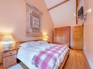 A bedroom with a bed, wooden wardrobe, and a television mounted on the wall.