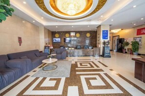 Um saguão de hotel com balcão de recepção, área de estar e um padrão decorativo no chão.