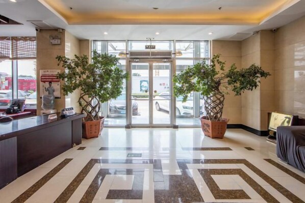 Un hall de hotel con una recepción, dos plantas en macetas, una puerta de cristal y un piso estampado.