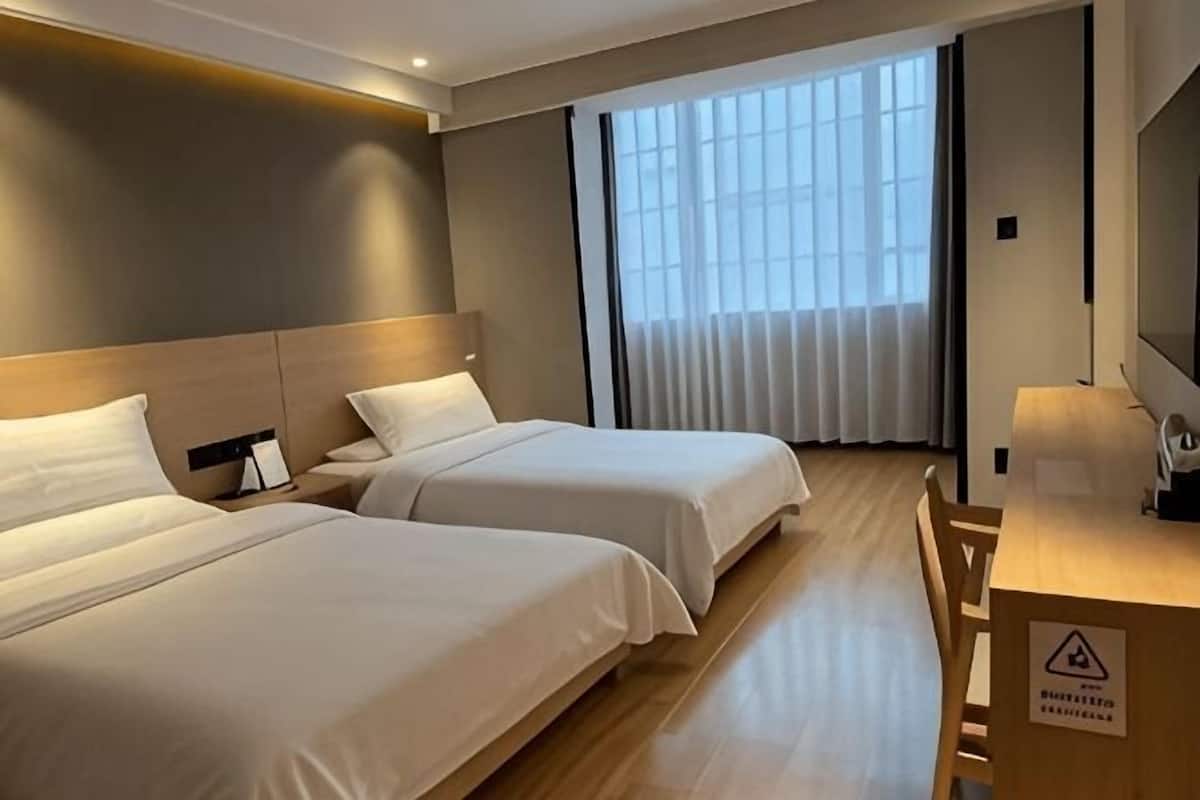 Quarto de hotel com duas camas, uma escrivaninha e uma janela grande com persianas.
