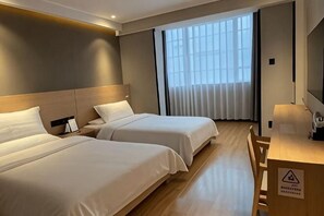 Une chambre d’hôtel avec deux lits, un bureau et une grande fenêtre avec des stores.