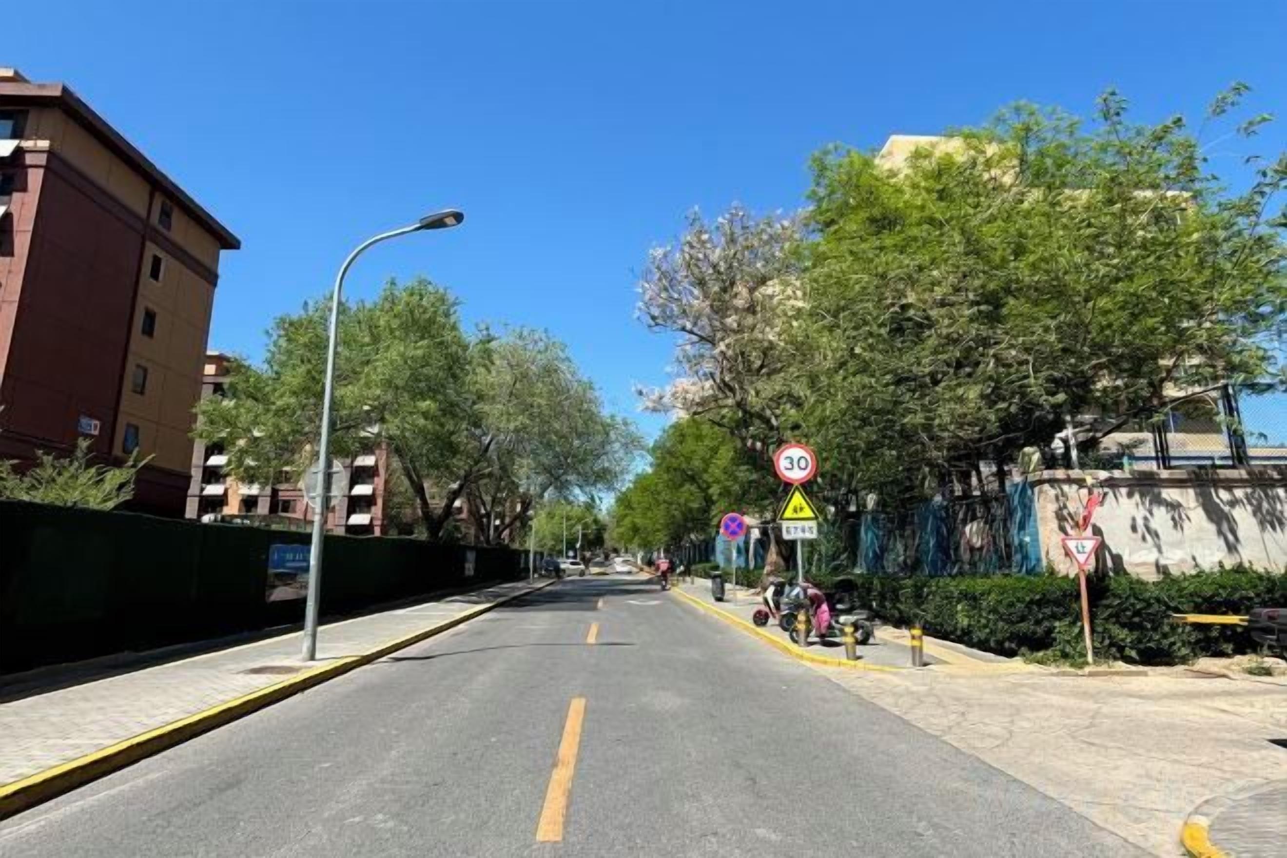 A street with a speed limit sign, a pedestrian crossing, and a clear sky.