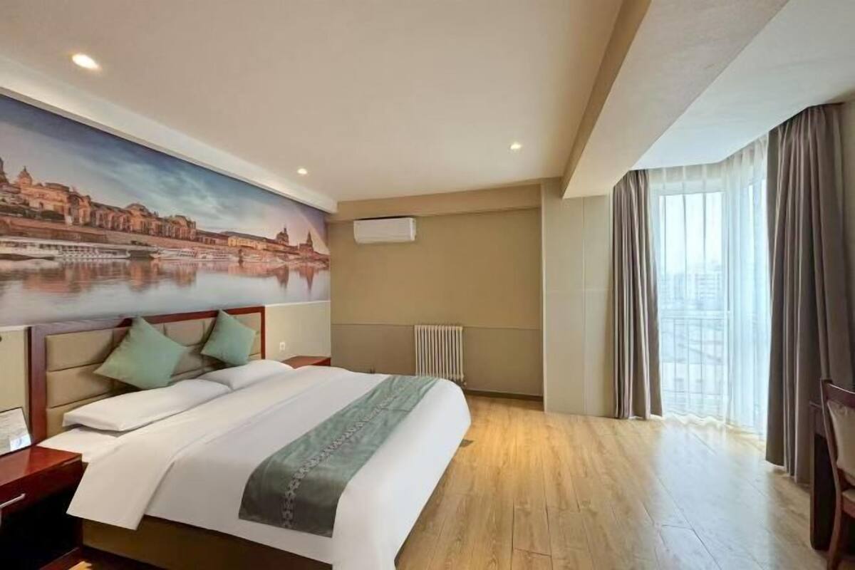 Quarto de hotel com cama, um mural da paisagem urbana, um radiador e uma janela com cortinas.