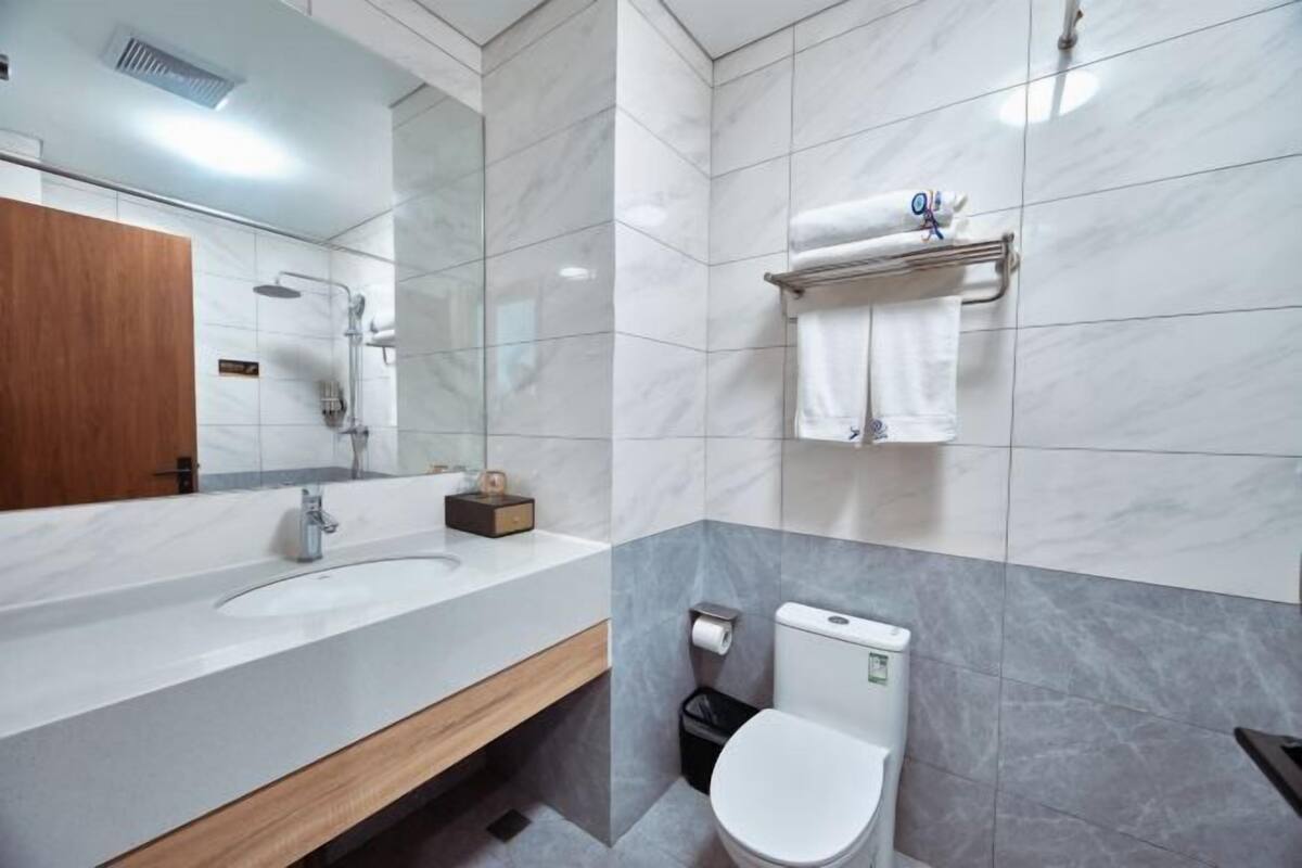 Uma casa de banho moderna com um espelho grande, uma pia, uma sanita e um porta-toalhas.
