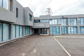 A modern building with a sign reading 'THE WORKS' and a parking area in front.