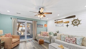 Un vaste salon doté d’un ventilateur de plafond, d’une porte-fenêtre coulissante donnant sur un espace extérieur et d’une décoration sur le thème de la marine.
