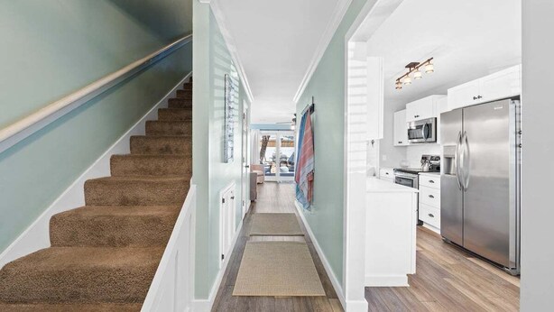 Un escalier menant à une cuisine avec des armoires blanches et des appareils électroménagers en acier inoxydable.