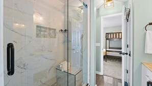 Une salle de bain moderne dotée d’une douche à parois de verre, d’un mur recouvert de carreaux de marbre et d’un banc en bois dans la pièce adjacente.