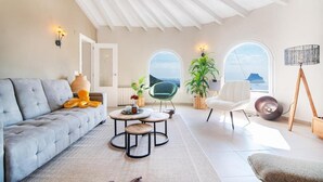 Un salon moderne avec un canapé, des tables rondes, un fauteuil vert et une vue à travers des fenêtres en arc de cercle.