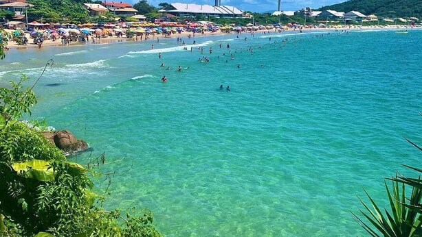 Une plage à l’eau turquoise et limpide, où l’on peut voir des gens se baigner, et une rangée de parasols de plage.
