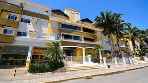 Un hôtel à plusieurs étages doté de balcons, de climatiseurs et d’une entrée sécurisée par un portail.