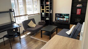A modern living room with a sofa, coffee table, and TV. There is a bookshelf with books and a decorative letter 'H'. - London Apartment - Sleeps 3-city Escape- Balcony (London)