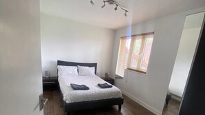 A bedroom with a bed, wooden flooring, a window with blinds, and a ceiling light fixture. - London Apartment - Sleeps 3-city Escape- Balcony (London)
