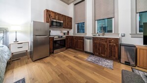 Cocina compacta con armarios de madera, refrigerador de acero inoxidable, microondas, horno y lavavajillas.