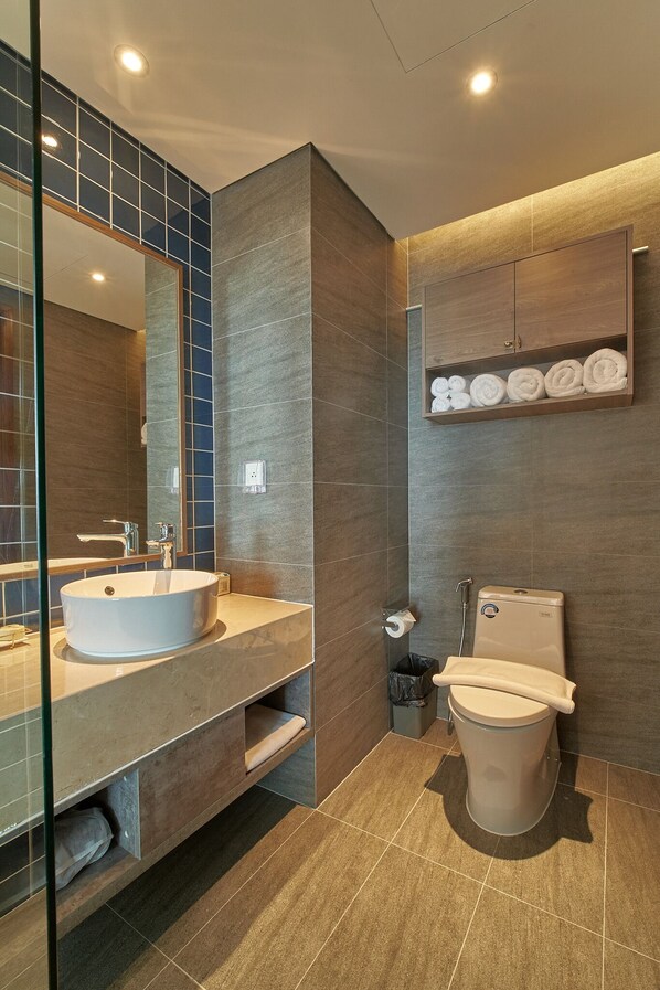 A modern bathroom with a large mirror, two sinks, a toilet, and a shelf with towels. - Mandala Nearly Beach - Condotel Apec Mui Ne (Mui Ne)