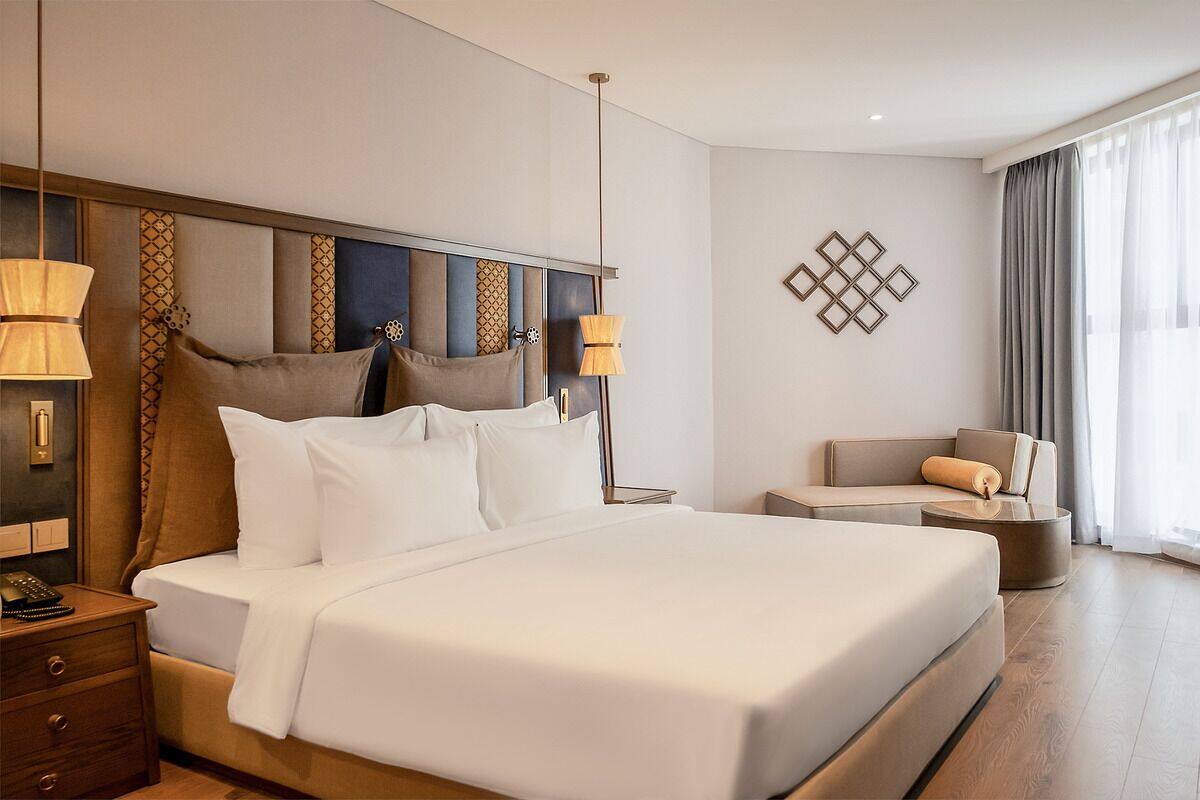 A modern hotel room with a large bed, bedside lamps, a sofa, and a decorative wall piece.