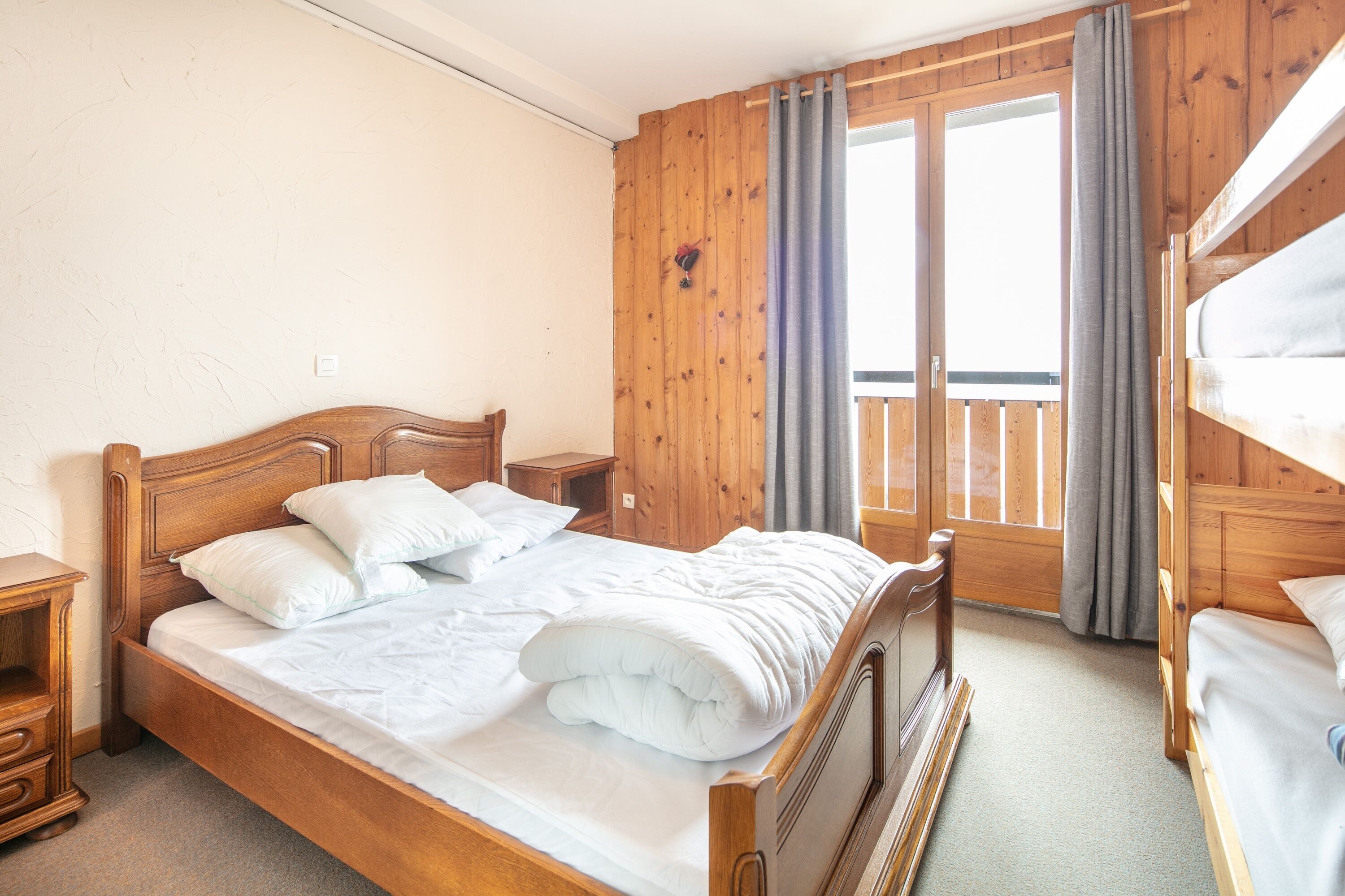 A wooden-framed bed with white bedding, a nightstand, and a window with curtains.