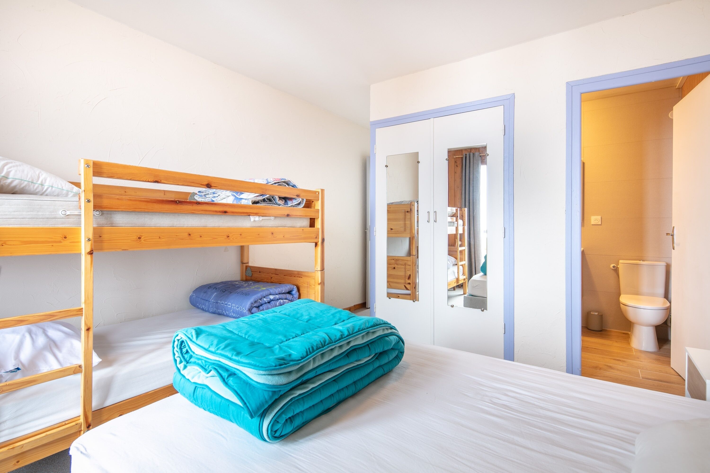 Een slaapkamer met een stapelbed, een kledingkast en een badkamer, zichtbaar door een geopende deur.