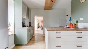 Une cuisine moderne avec des meubles de couleur vert clair, un plan de travail en bois et une horloge bien visible au mur.