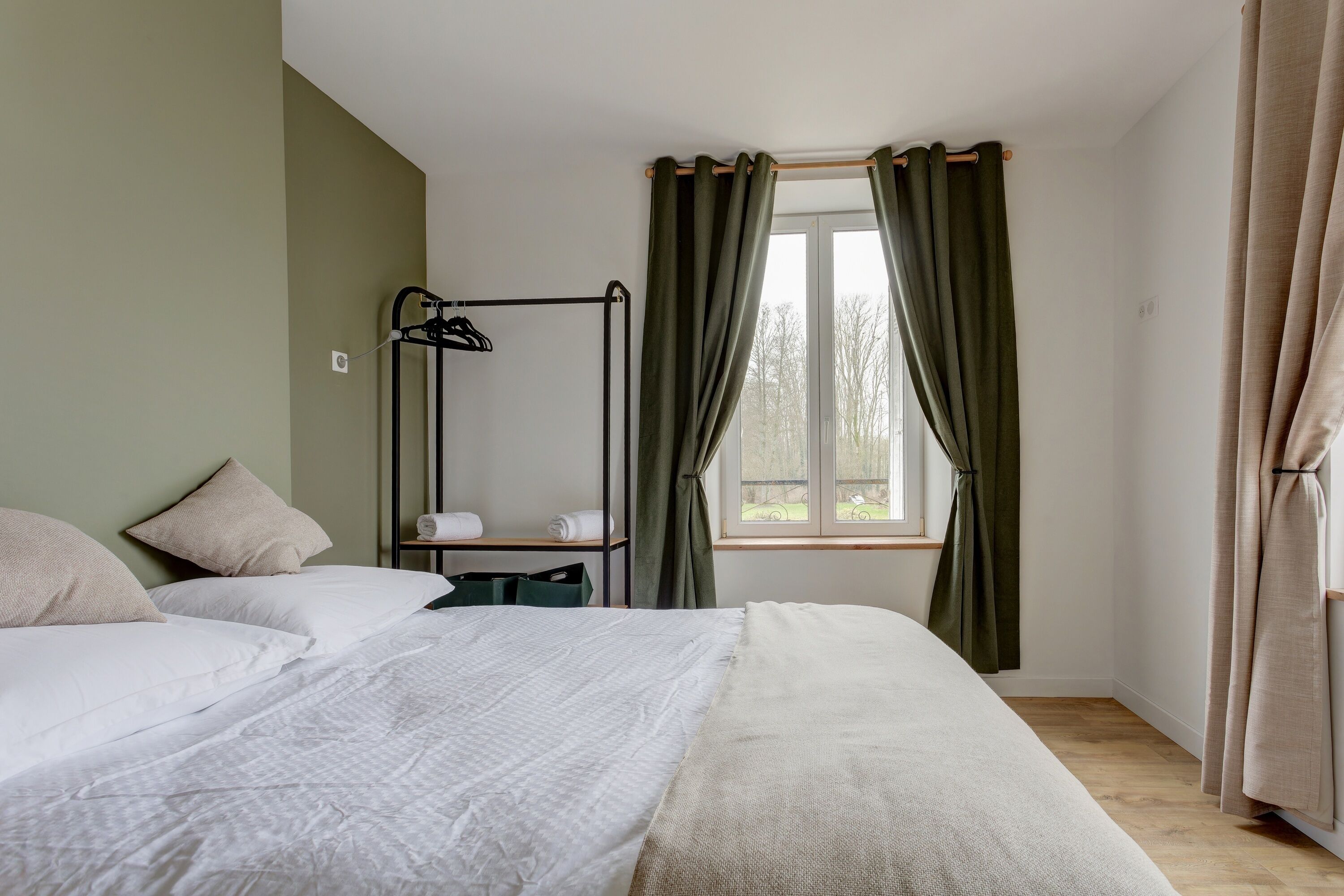 Une chambre à coucher avec un lit, une table de chevet, une fenêtre avec des rideaux et un radiateur.