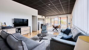 A modern living room with a large flat-screen TV, grey sofas, a coffee table, and a dining area with a table and chairs. - La Bouteille à la Mer, Maison d'architecte avec jacuzzi (Barneville-Carteret)