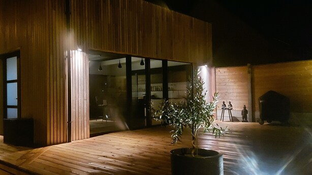 A modern building with a wooden facade, large glass windows, and a wooden deck area with a potted plant. - La Bouteille à la Mer, Maison d'architecte avec jacuzzi (Barneville-Carteret)