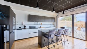 A modern kitchen with a central island, bar stools, and a sliding glass door leading to an outdoor patio. - La Bouteille à la Mer, Maison d'architecte avec jacuzzi (Barneville-Carteret)