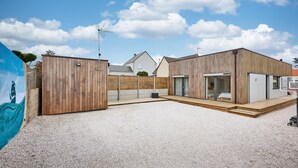A modern building with a wooden facade, a covered outdoor area, and a visible door. - La Bouteille à la Mer, Maison d'architecte avec jacuzzi (Barneville-Carteret)