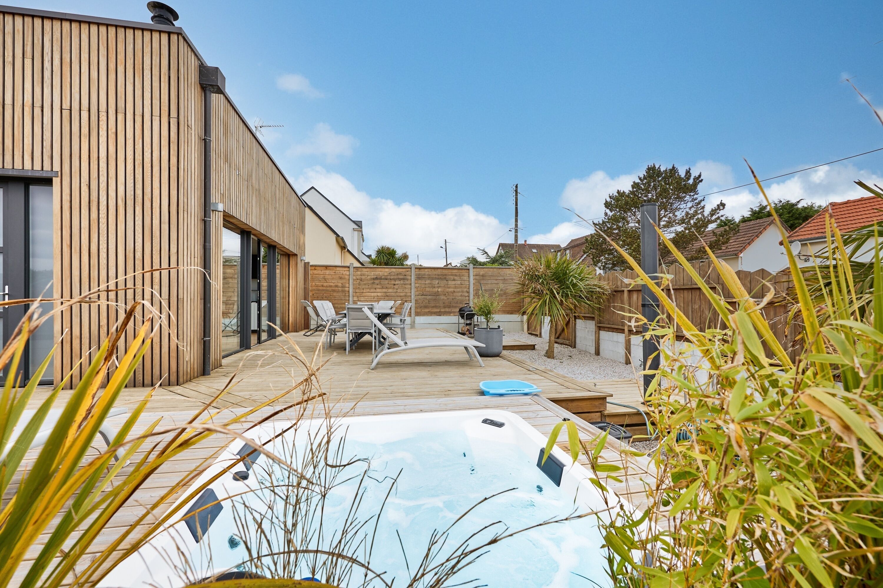 Ein modernes Haus mit Holzfassade, einem Whirlpool und Gartenmöbeln.