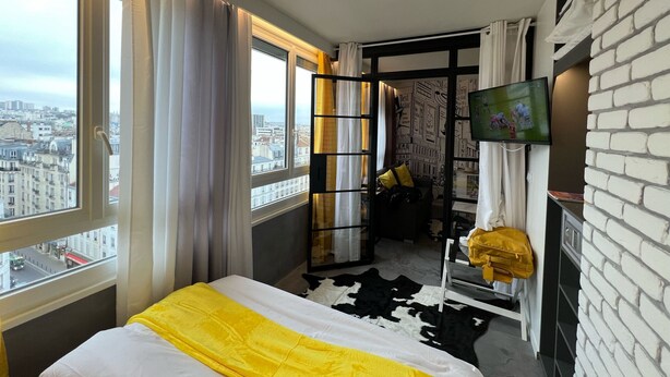Une chambre d’hôtel avec un lit, une télévision, une vue sur la ville, un mur en briques et une fenêtre avec des rideaux.