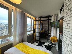 Une chambre d’hôtel avec un lit, une télévision, une vue sur la ville, un mur en briques et une fenêtre avec des rideaux.