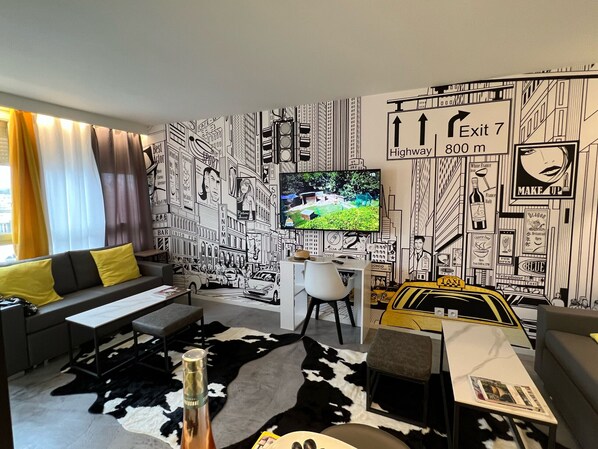 Una sala de estar moderna con un mural de un paisaje urbano, un televisor de pantalla plana, un sofá, una mesa de centro y una botella de vino.