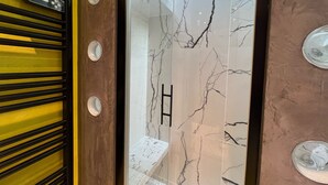 Une salle de bain avec une porte en verre, des murs en marbre et un porte-serviettes noir.