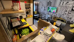 Une cuisine moderne avec un coin repas, un téléviseur et un mur décoré d’illustrations représentant des paysages urbains.