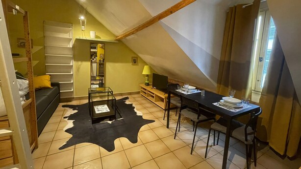Een knus zolderkamer met schuine wanden, een bed, een bureau met stoel, en een eettafel gedekt voor twee personen.