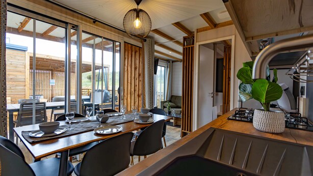 Un comedor con una mesa de madera dispuesta para cuatro, una lámpara colgante moderna y vistas al exterior.
