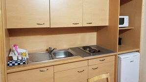 Una cocina compacta con gabinetes de madera, un lavamanos, una estufa y un microondas.