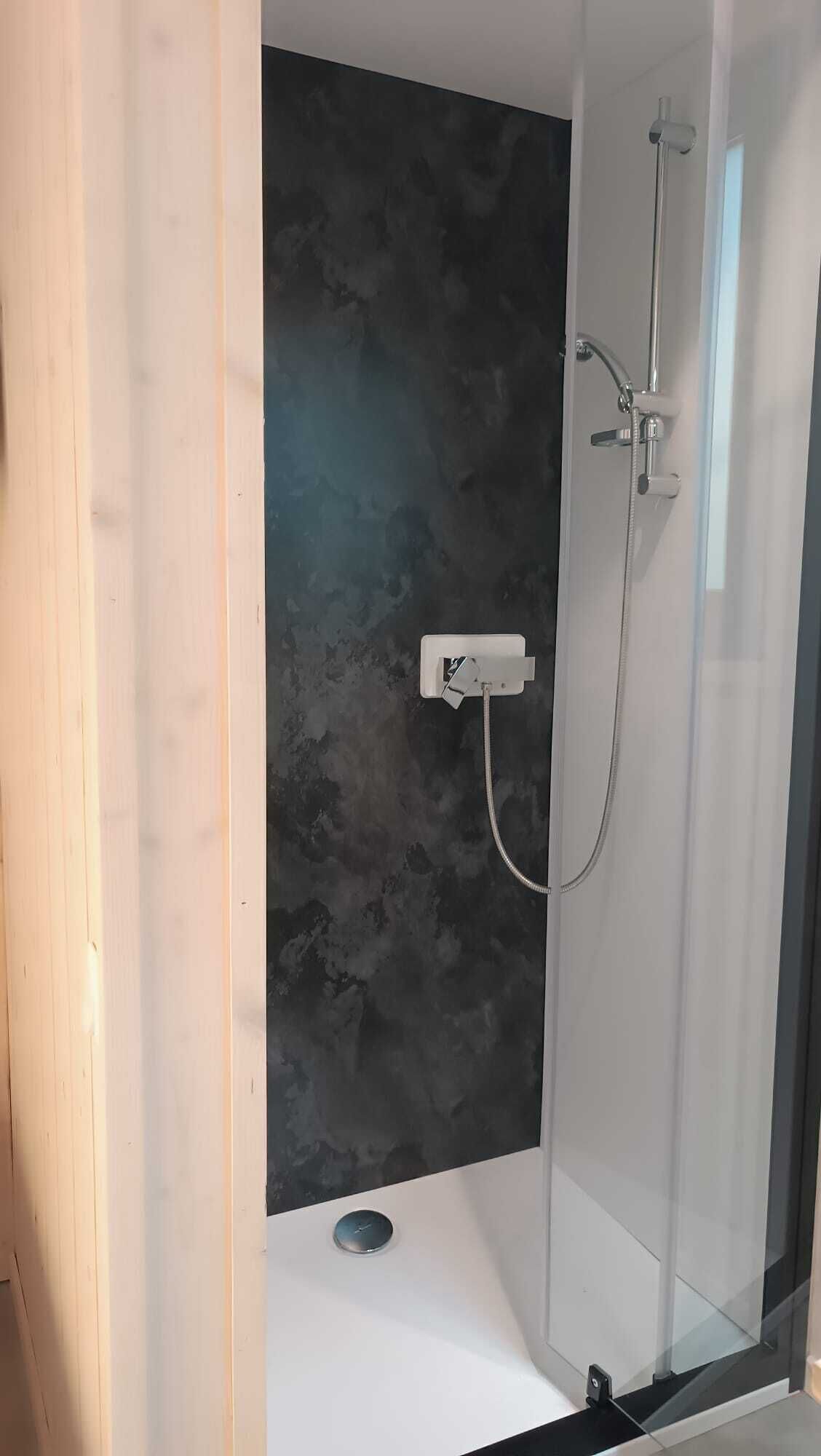 A modern shower with a glass enclosure, a dark textured wall, and a white base.