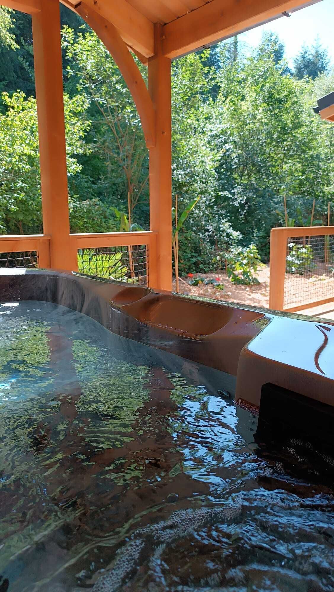 A hot tub area with a wooden structure overhead and a garden view.