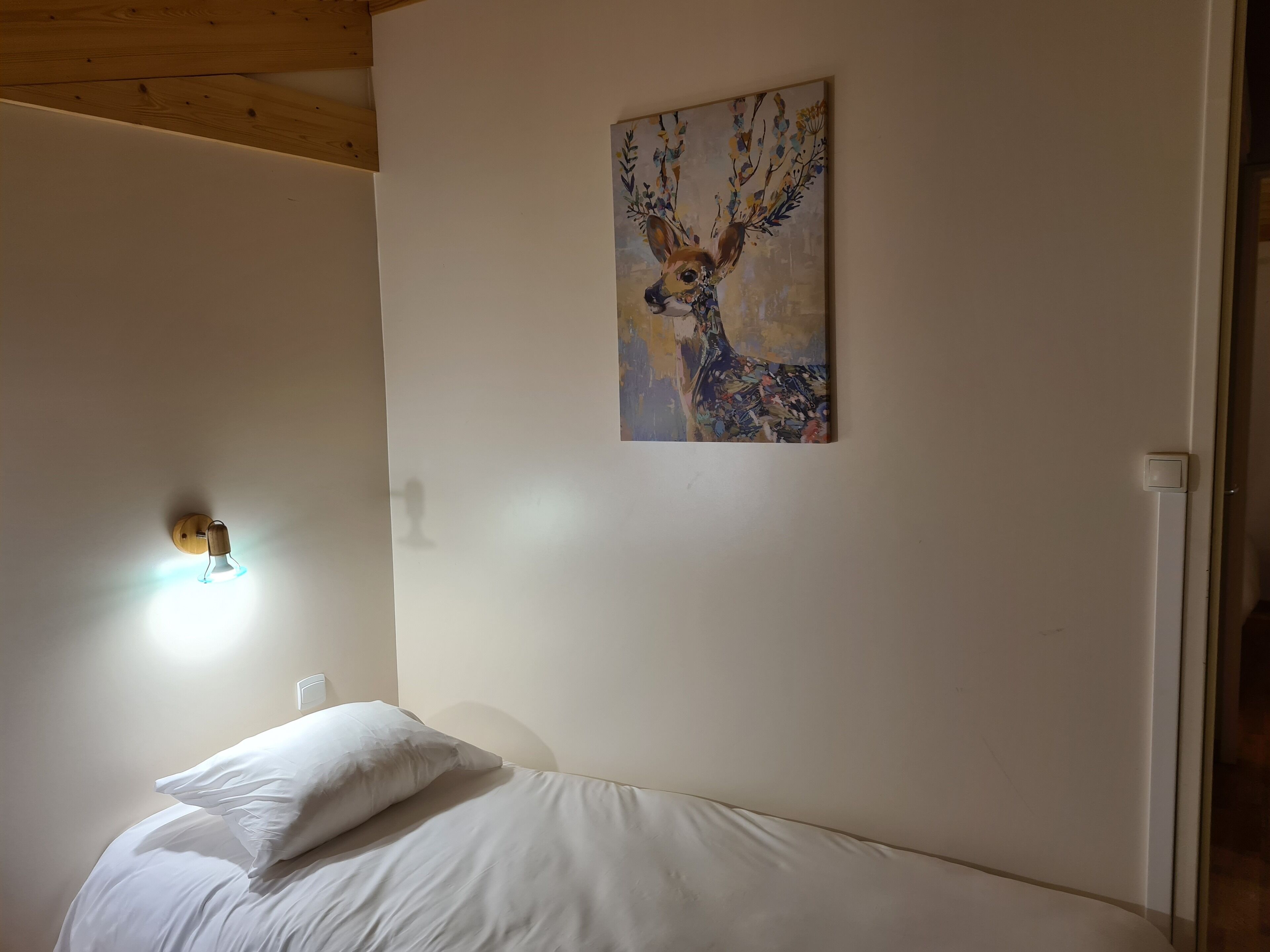 A bedroom with a bed, a wall-mounted light, and a painting of a deer.