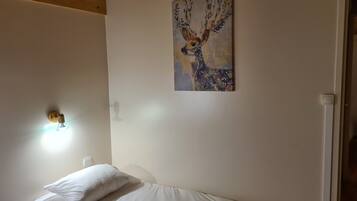 A bedroom with a bed, a wall-mounted light, and a painting of a deer.