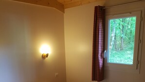 Una cama individual con sábanas blancas en una habitación con techo de madera y ventana con cortinas.