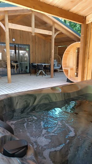 A wooden outdoor seating area with tables and chairs, a hot tub, and a glass door leading to a covered patio.