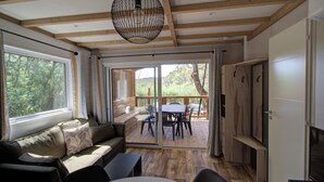 Una habitación acogedora con techo de madera, un sofá con cojines, una mesa de comedor con sillas y una puerta corredera de vidrio que da a una terraza exterior.