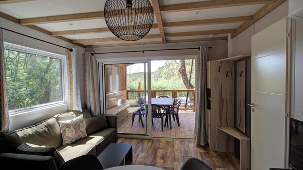 A cozy room with a wooden ceiling, a sofa with cushions, a dining table with chairs, and a sliding glass door leading to an outdoor deck.