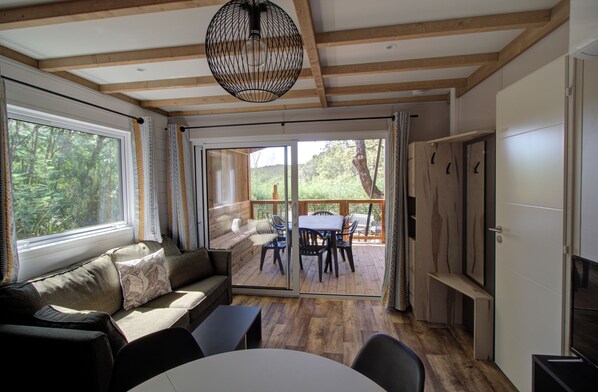 A cozy room with a wooden ceiling, a sofa with cushions, a dining table with chairs, and a sliding glass door leading to an outdoor deck.