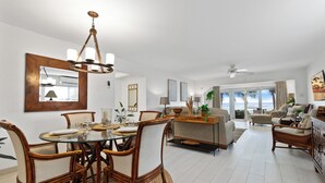 Een ruime woonkamer met een eethoek, grote ramen en een plafondventilator.