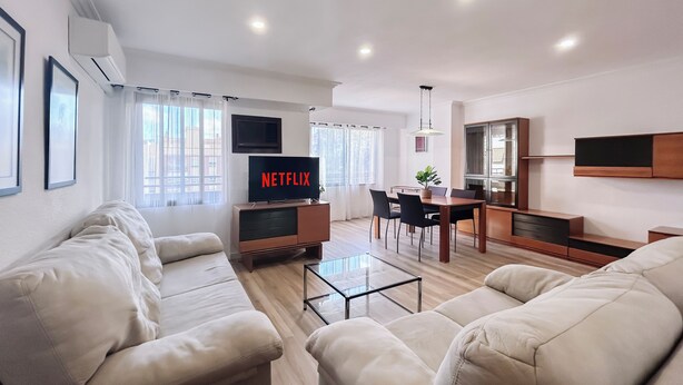 A modern living room with a flat-screen TV, a dining area, and a kitchen.